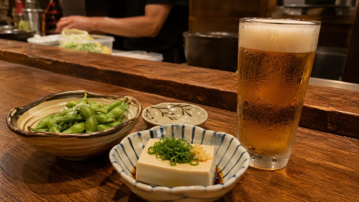 Edamame, chilled tofu, and a cold beer on the wooden counter of a Japanese izakaya
