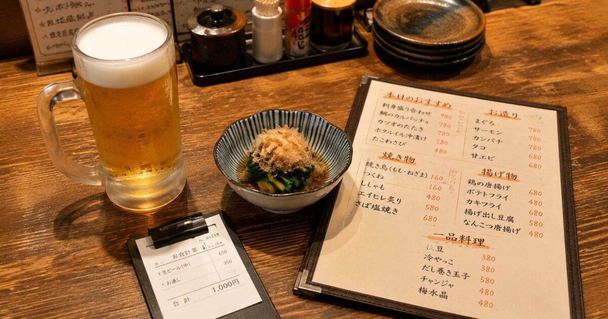 A typical izakaya table in Japan with beer, an otoshi appetizer, a menu, and a receipt
