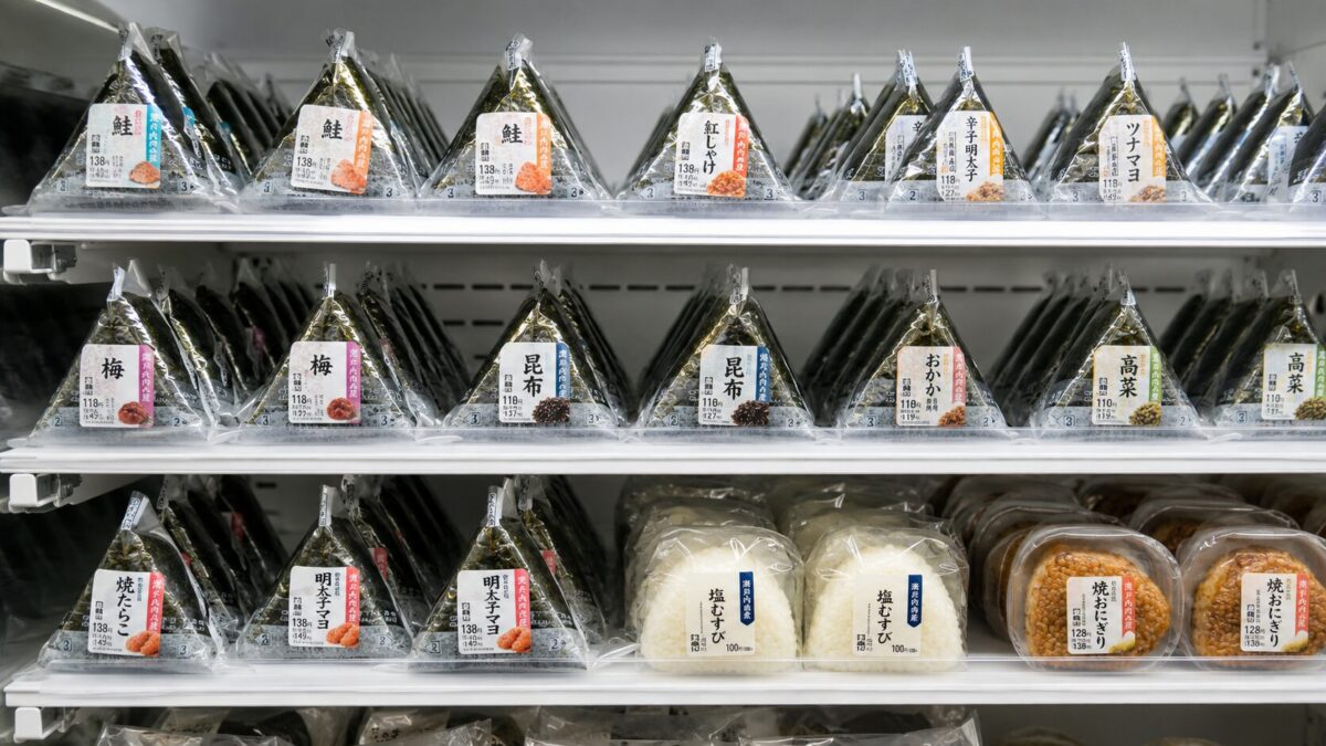 Japanese convenience store shelf filled with onigiri labeled salmon, pickled plum, kombu, and tuna mayonnaise