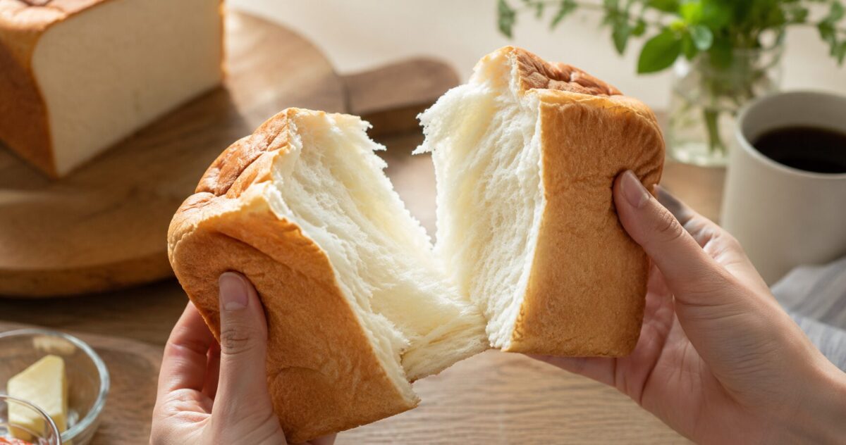 Hands pulling apart a loaf of fluffy Japanese shokupan to reveal its soft, airy texture.