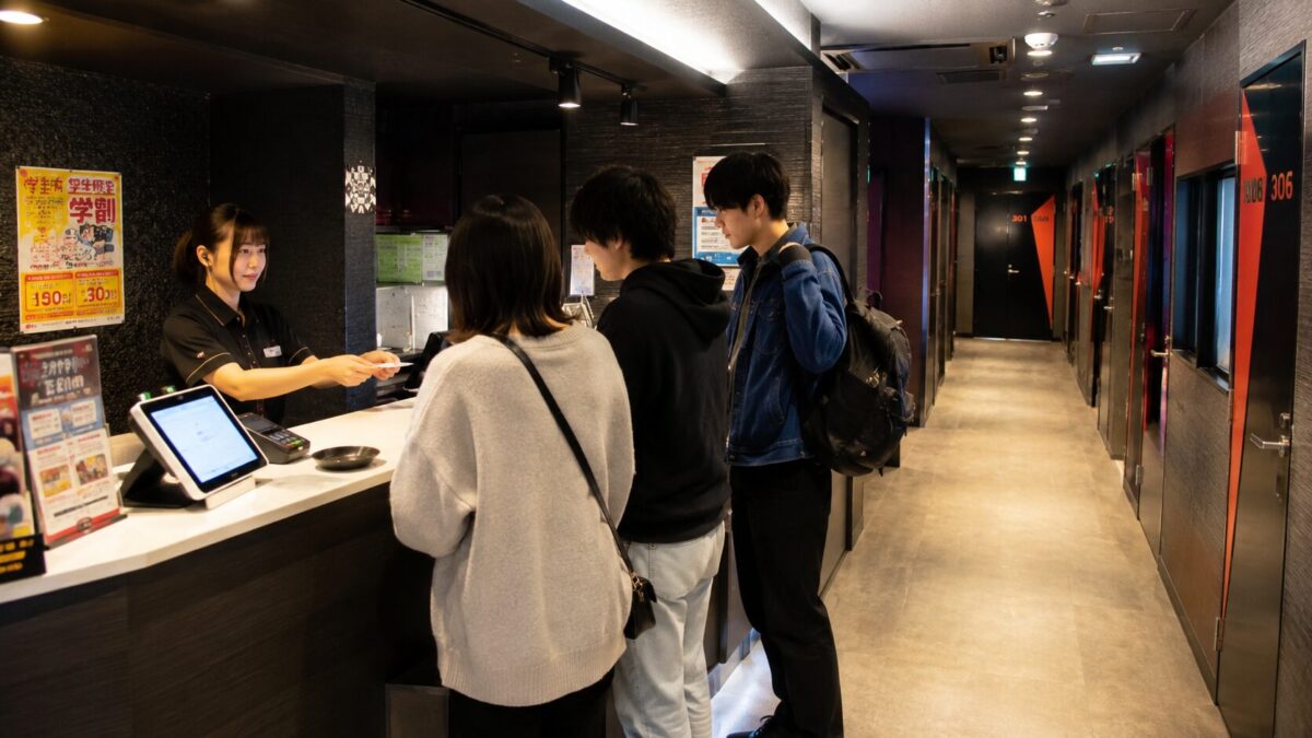 Customers checking in at a Japanese karaoke reception with private rooms visible along the hallway