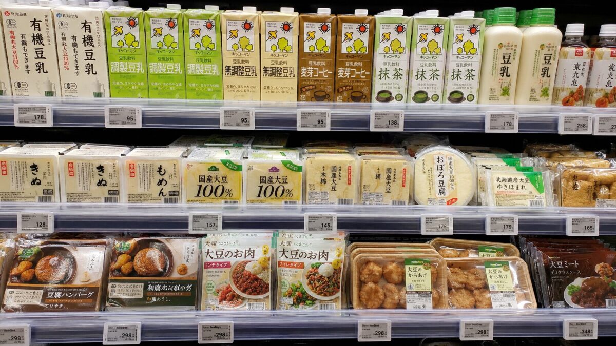 Japanese supermarket shelf stocked with soy milk, tofu, soy meat, and tofu hamburger products