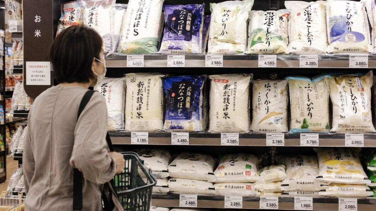 A shopper looking at bags of rice and prices in a Japanese supermarket